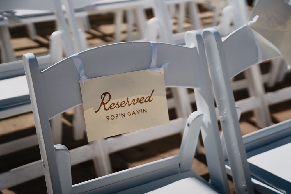 White folding chairs with a reserved sign for Robin Gavin at an outdoor wedding ceremony.