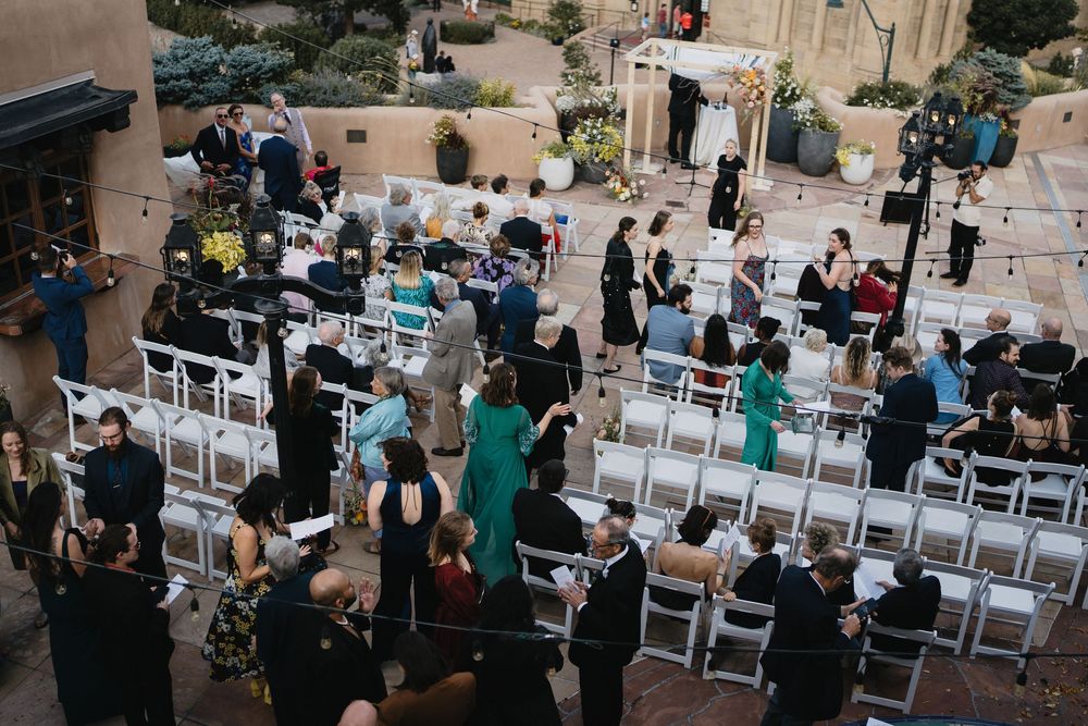 Aerial view of an outdoor wedding ceremony with white chairs and guests mingling in a courtyard.