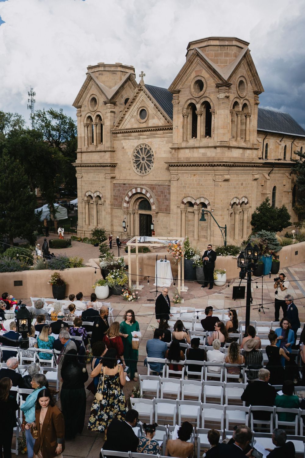 Outdoor wedding ceremony at Cathedral Basilica of Saint Francis of Assisi in Santa Fe, New Mexico, with guests seated in white chairs.