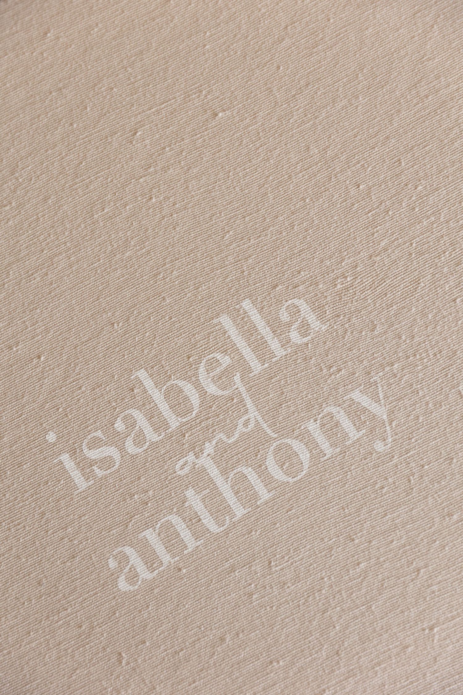 Elegant embossed wedding stationery with names Isabella and Anthony on textured beige paper.