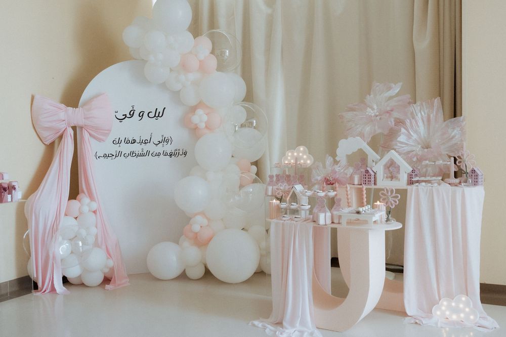 Elegant baby celebration backdrop with a pink and white balloon arch and dessert tables