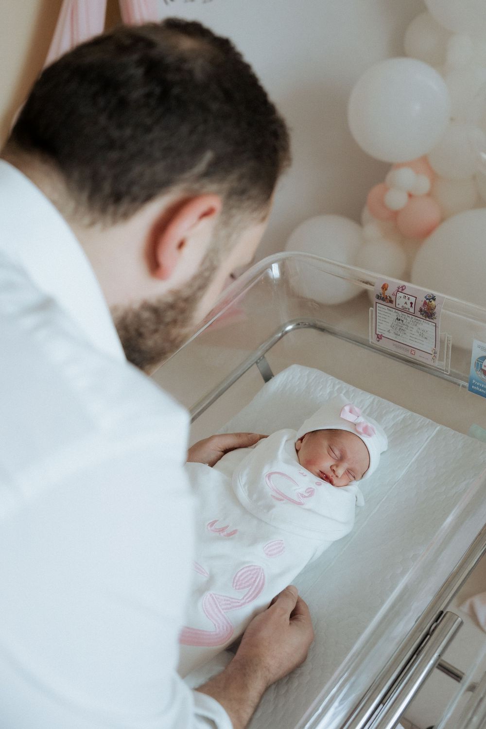 Father gazing at his newborn resting in a bassinet beside soft balloon decor