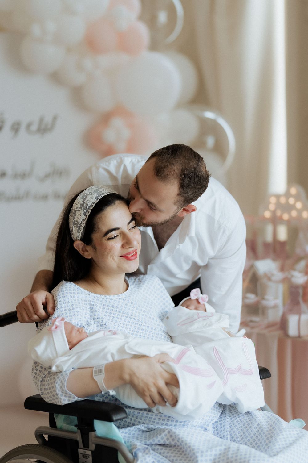 Father kissing mother's forehead as she cradles their newborn at a family celebration