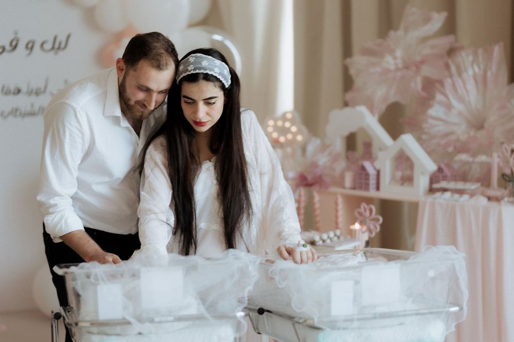 Parents in white admiring their newborns in decorated bassinets at a pink baby celebration