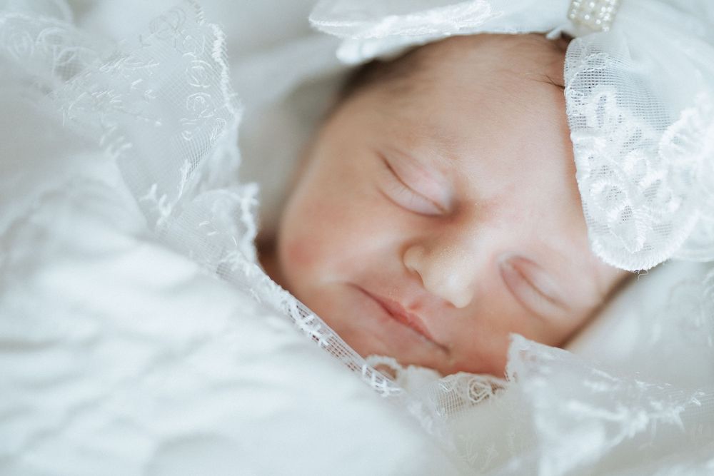 Newborn baby sleeping peacefully in white lace bedding wearing a delicate headband
