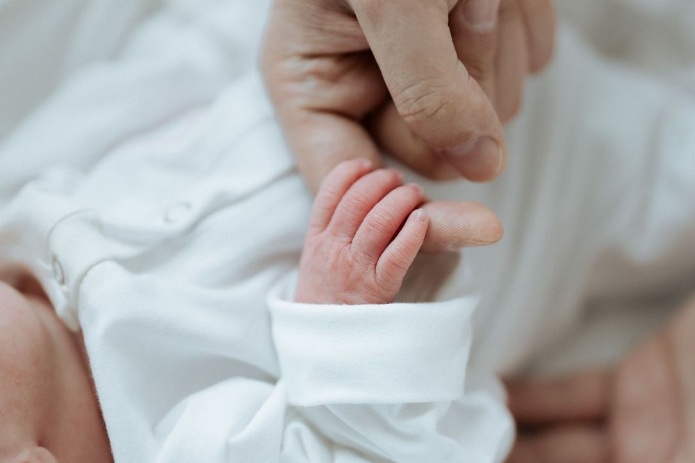 Newborn baby's tiny hand gripping an adult's finger in a tender close-up