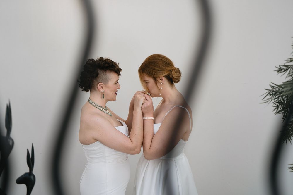Two brides in white dresses hold hands tenderly, sharing an intimate moment on their wedding day.