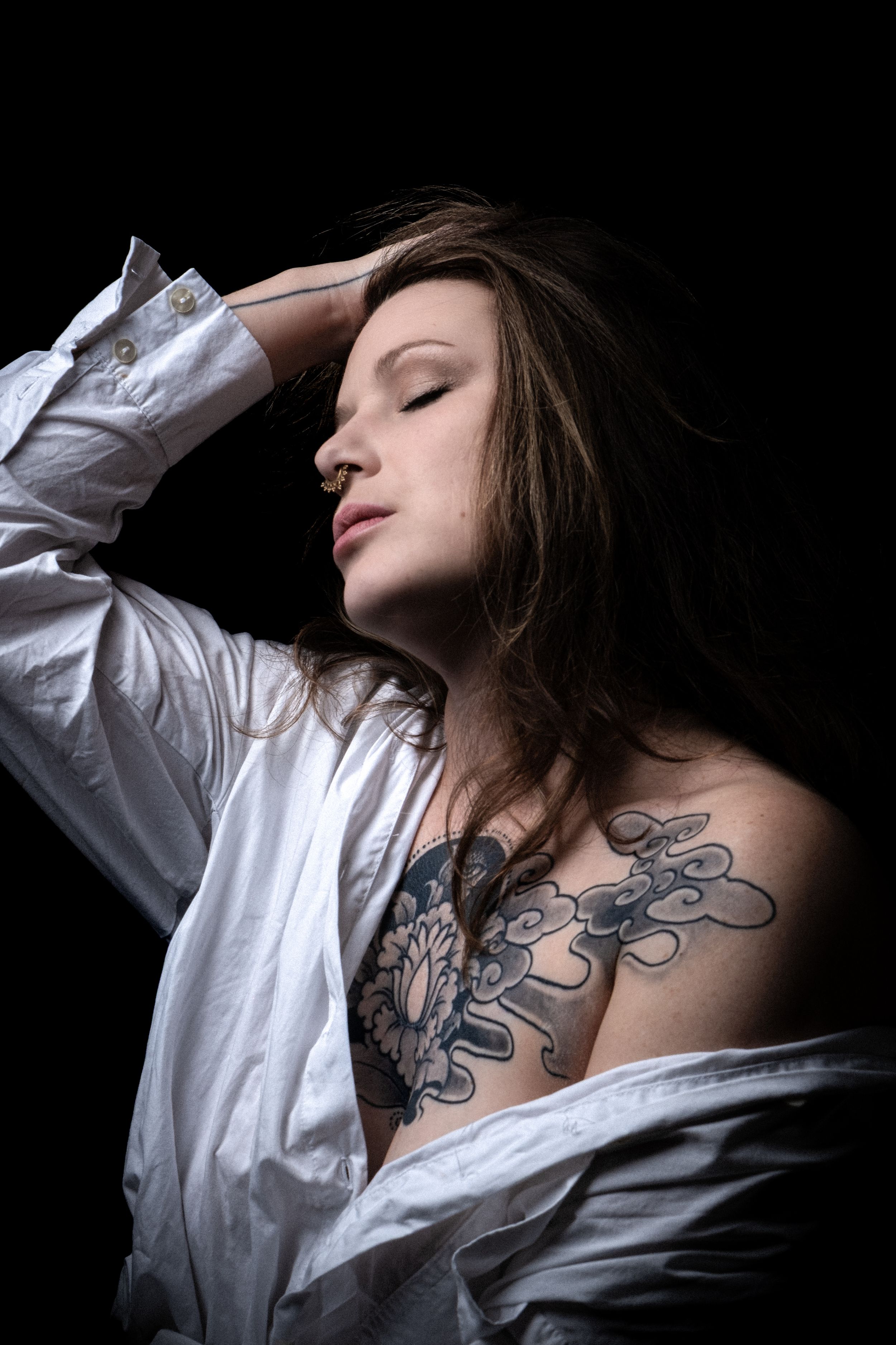 Portrait studio d'une femme tatouée éclairée sur fond noir.