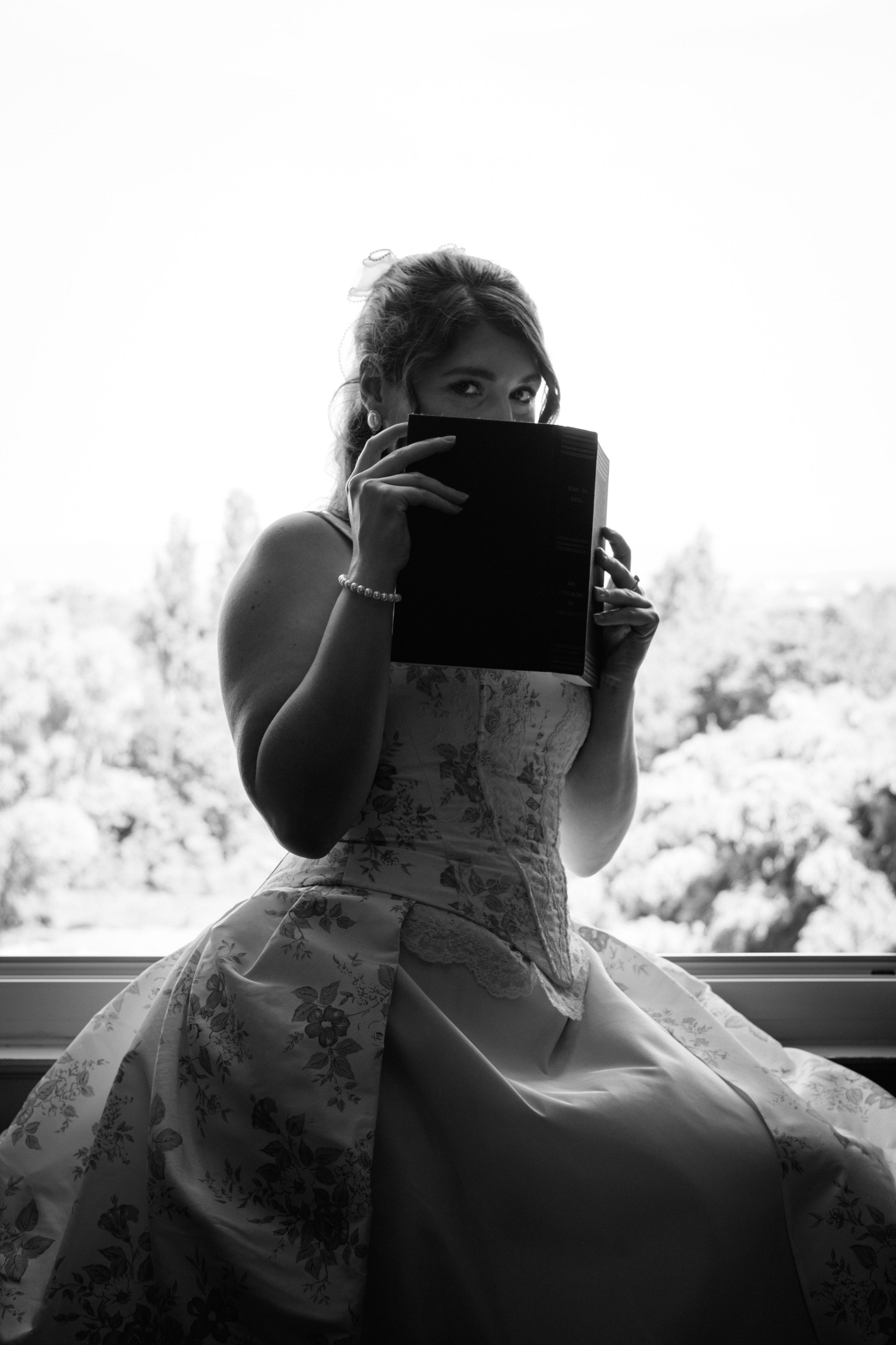 Portrait en noir et blanc d'une femme lisant près d'une fenêtre lumineuse.