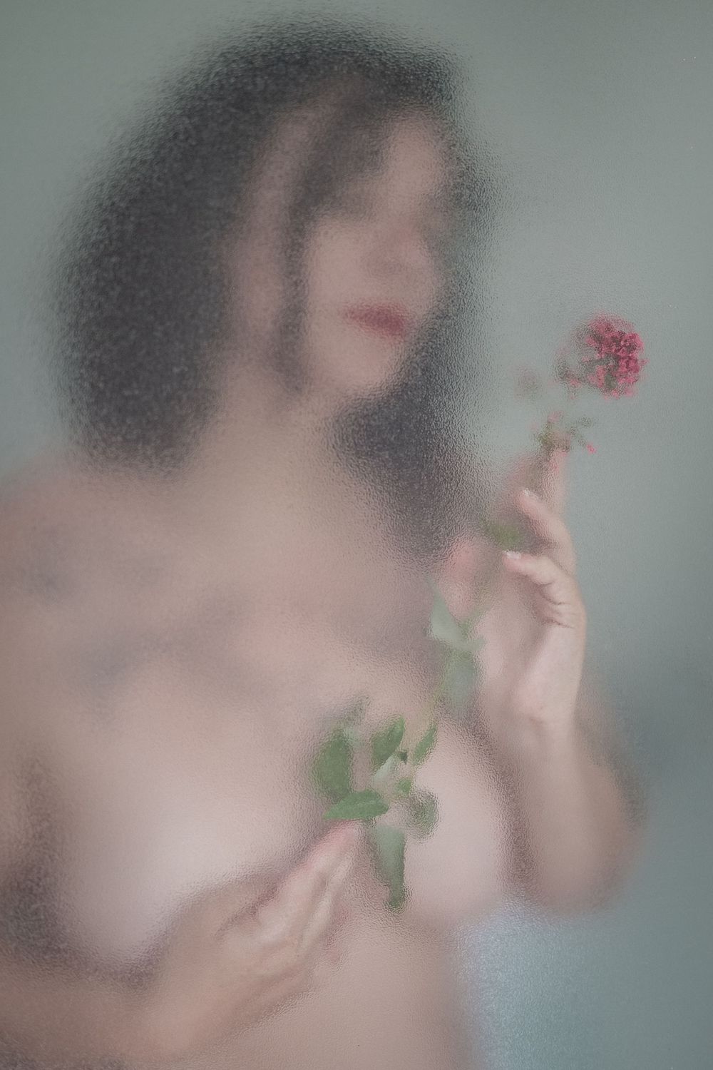 Portrait artistique réalisé à travers une parois de douche avec une fleur tenue à la main.