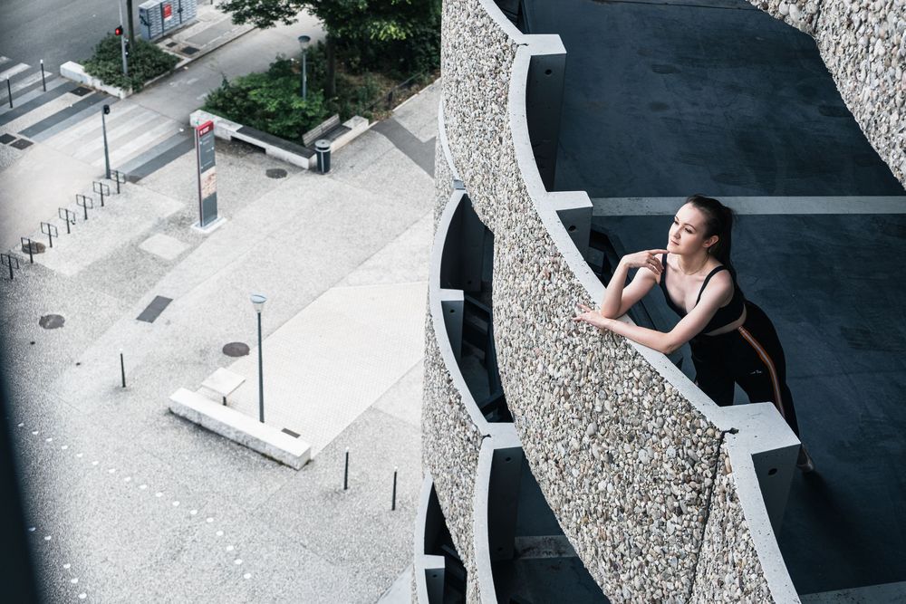 Portrait environnemental d'une danseuse sur un balcon d'architecture contemporaine.