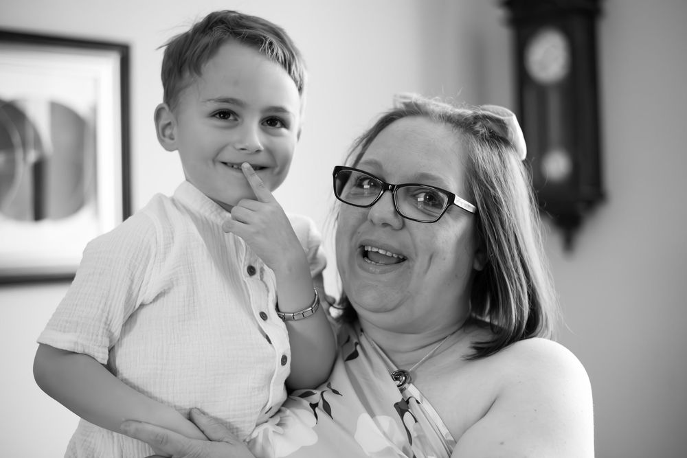Black and white photo of a smiling woman holding a young boy, both happy indoors near a clock.