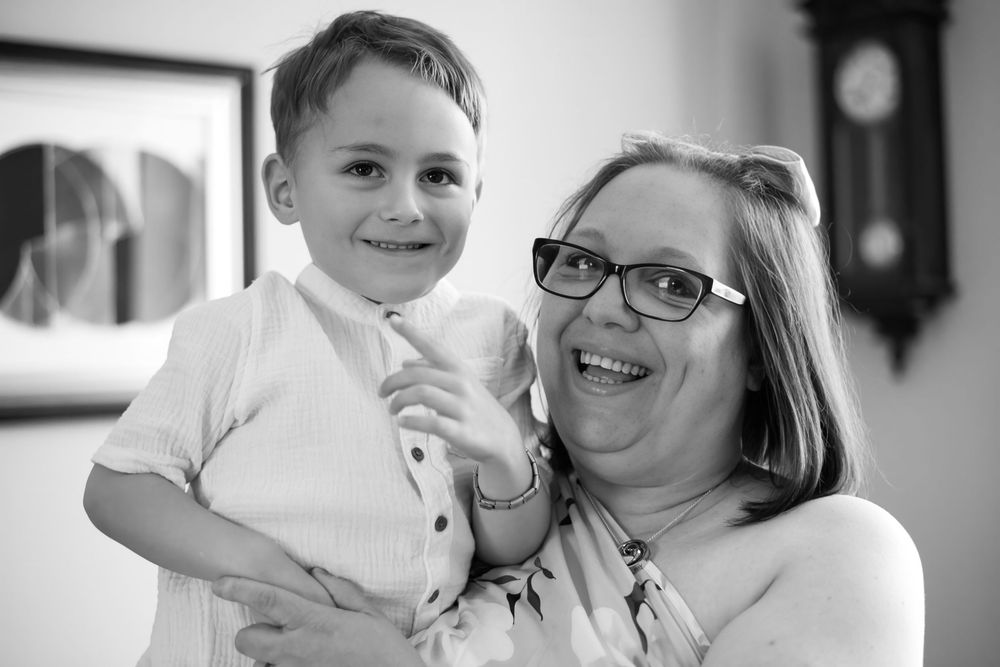 Black and white photo of a smiling woman with glasses holding a happy young boy in a white shirt and tie.