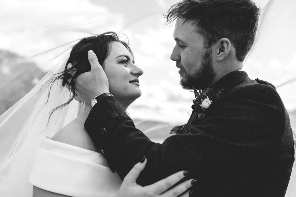 Black and white romantic portrait of bride and groom embracing, veil blowing in wind at Scottish wedding.