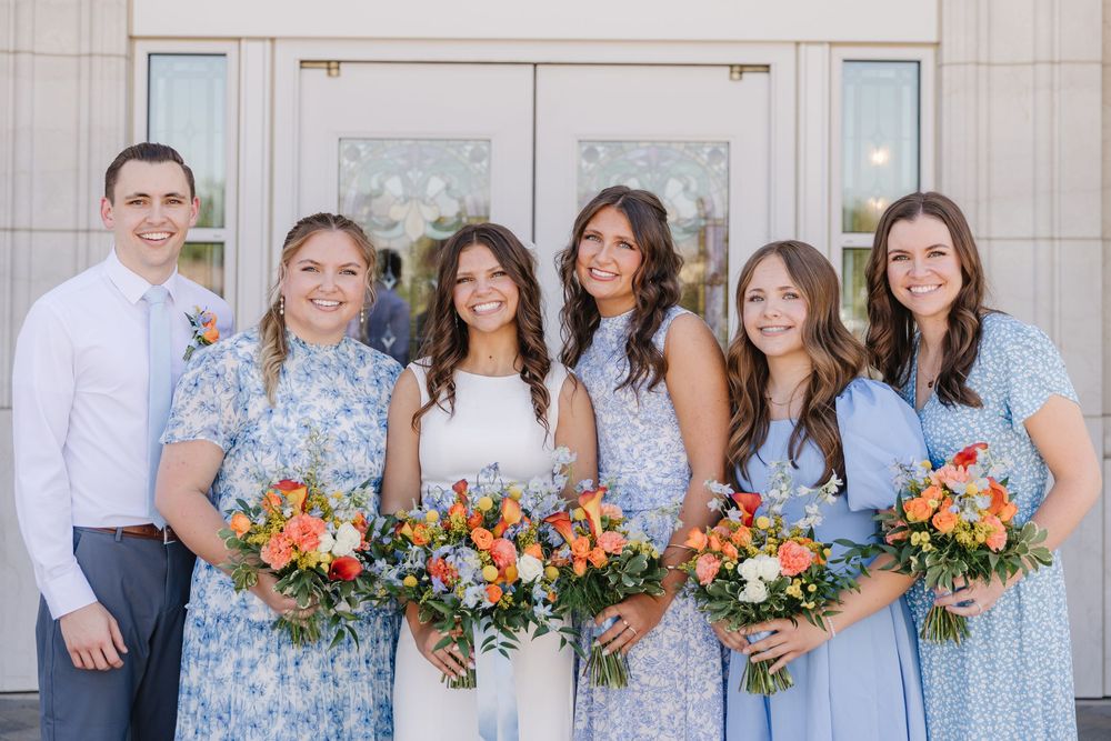 Bride with bridesmaids in blue floral dresses holding colorful bouquets outside temple.