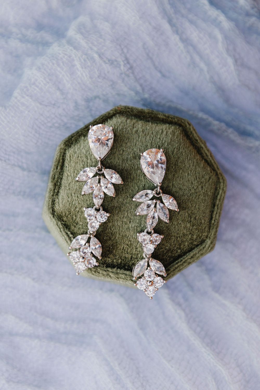 Elegant crystal drop earrings with pear and leaf-shaped stones displayed on a green velvet jewelry box.