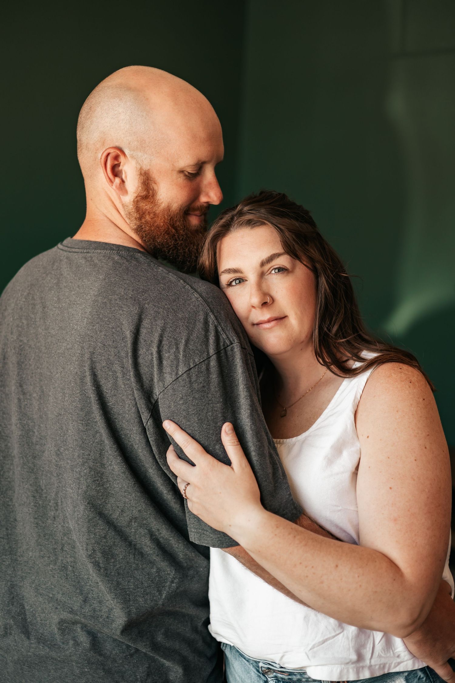 A woman in a white tank top rests her head on a bearded bald man's shoulder in a tender embrace | Anniversary Photos in Johnston, Colorado