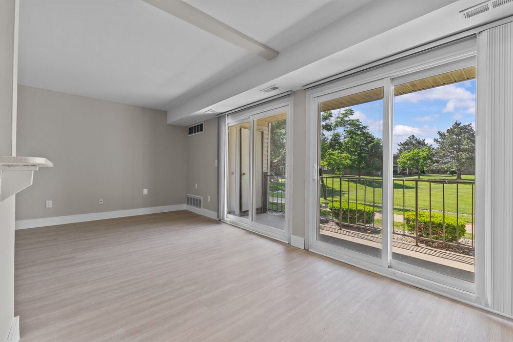 Bright living room with large sliding glass doors overlooking a lush green backyard, featuring light hardwood floors and neutral walls.