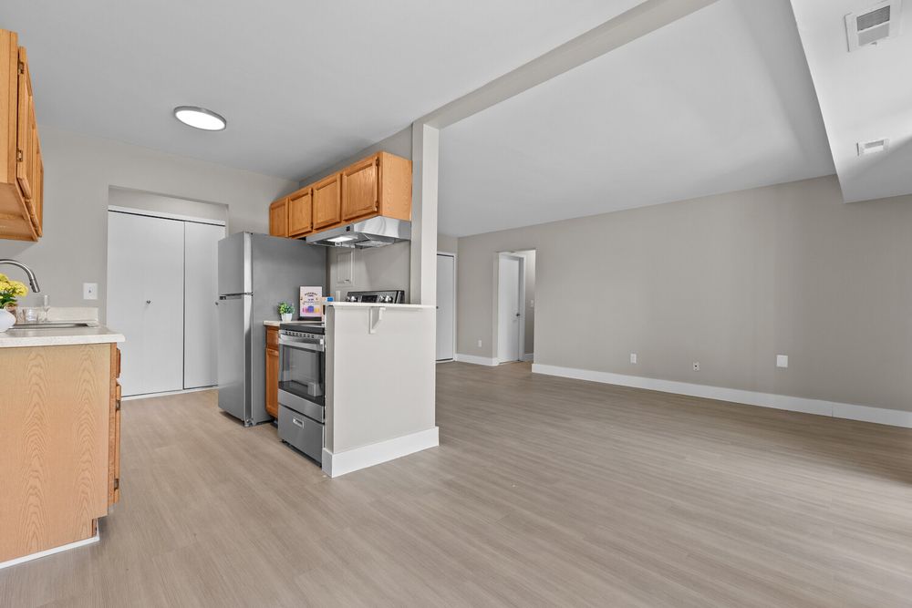Open-concept kitchen with stainless steel appliances, oak cabinets, and light wood flooring flowing into a spacious living area.