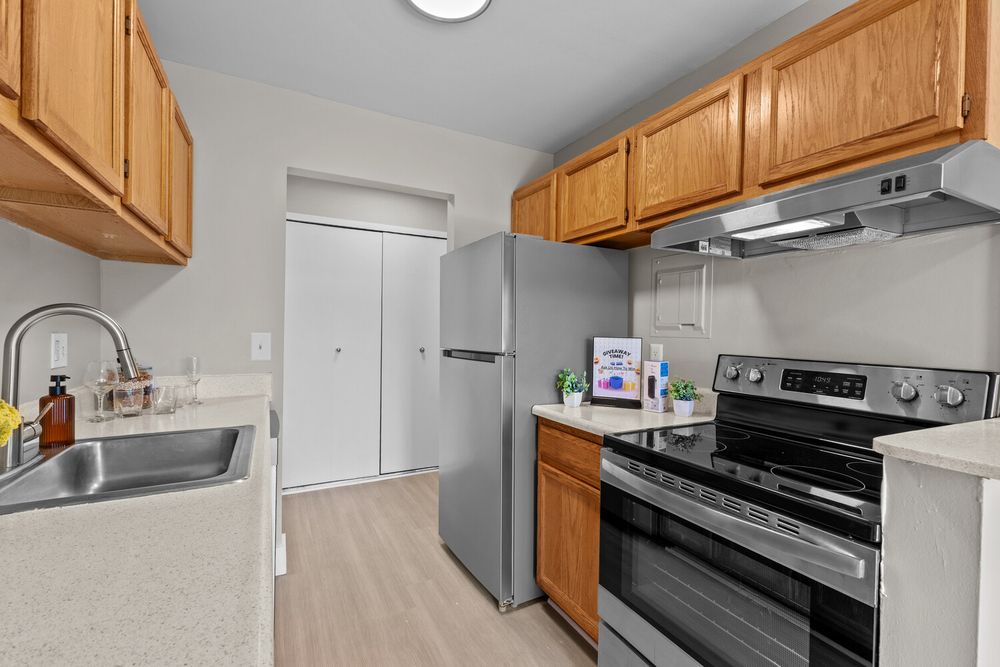 Modern kitchen with stainless steel appliances, oak cabinets, and light countertops in a bright apartment.