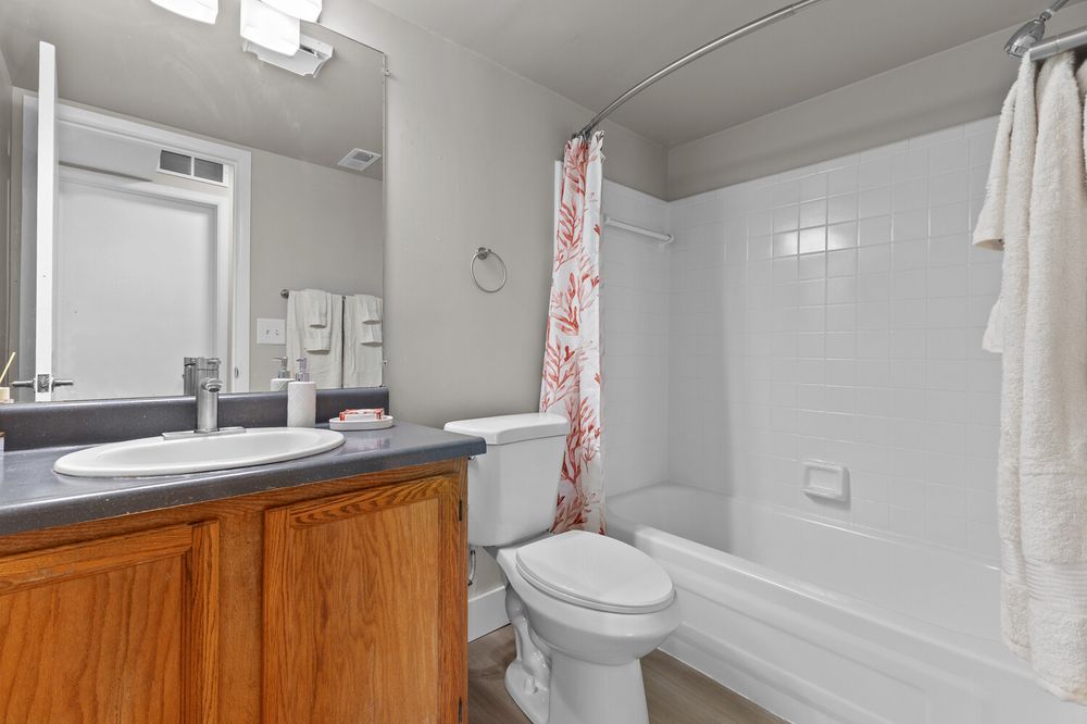 Clean bathroom featuring a single-sink vanity with wood cabinets, toilet, and tiled shower-tub combo with a red curtain.