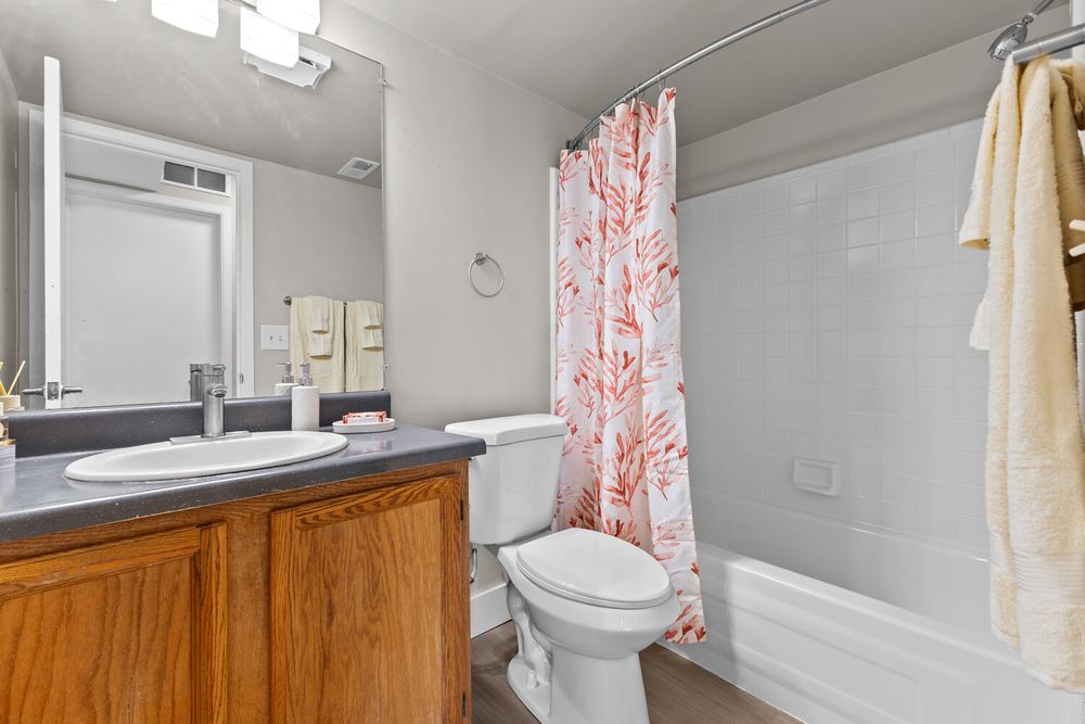 Bathroom with wooden vanity, large mirror, white toilet, and tub with red floral shower curtain.