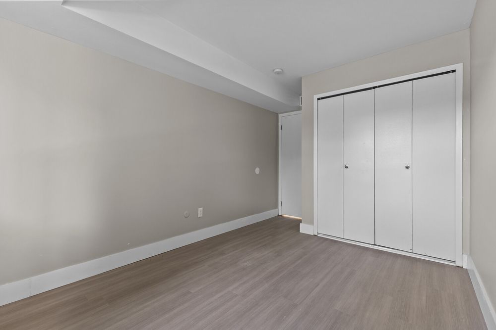 Empty bedroom with light gray walls, white bifold closet doors, and modern laminate hardwood flooring.