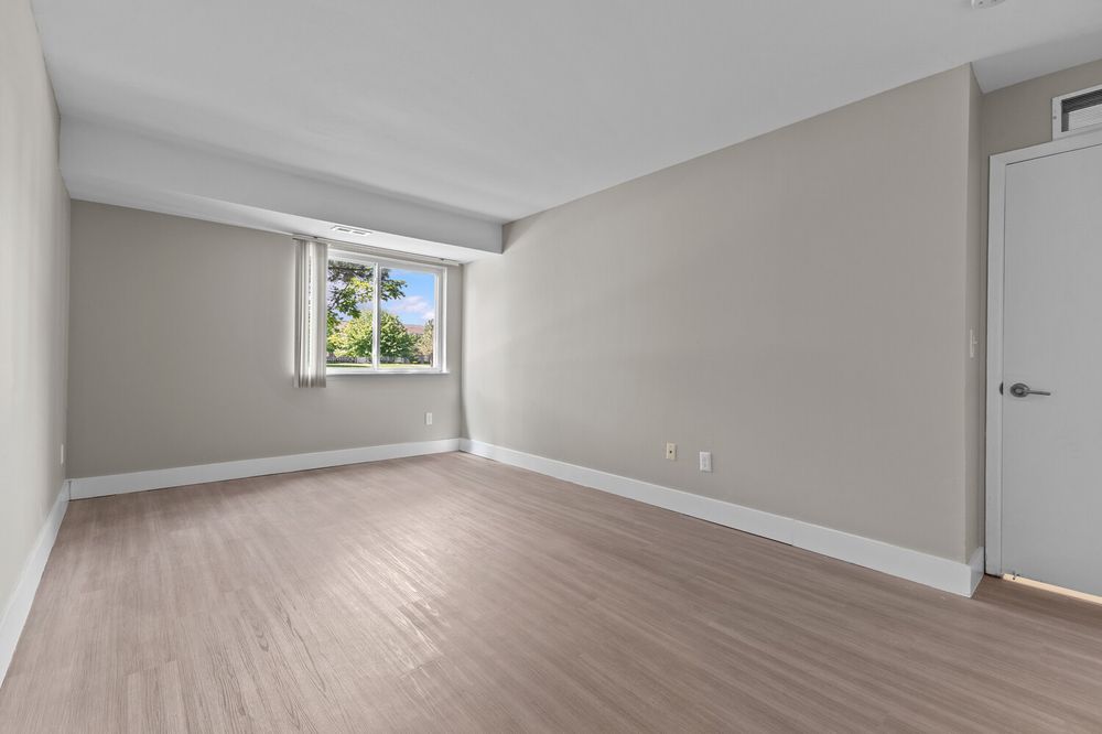 Spacious empty bedroom with light hardwood floors, gray walls, and a bright window with a door.