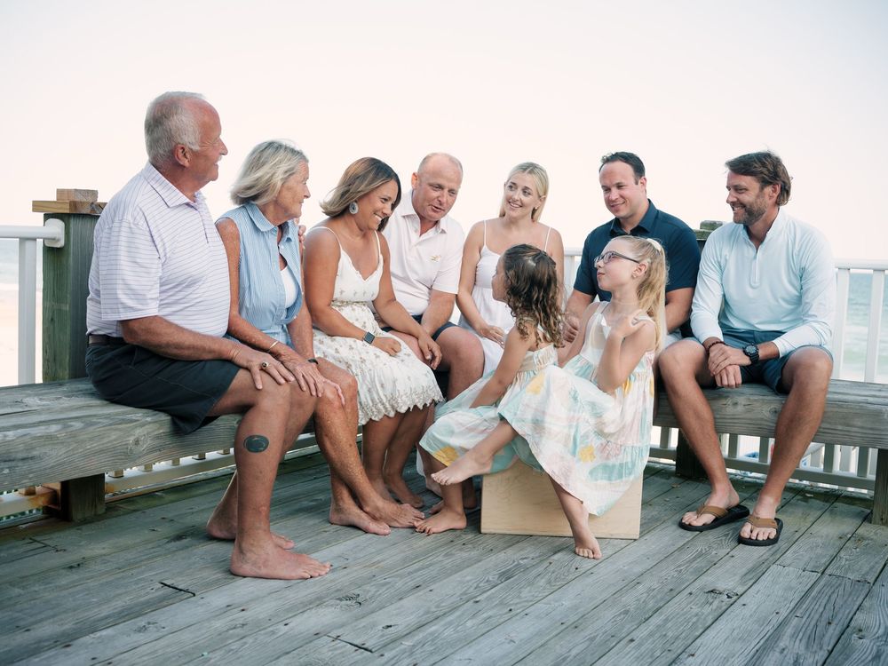 Happy family group sitting together on a wooden deck near the beach during a golden hour photo session.