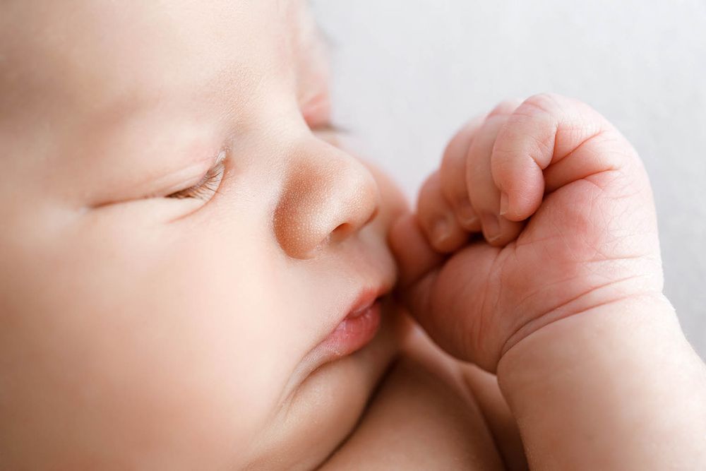 Close-up of a peaceful sleeping newborn baby with tiny fist near face on soft white background.
