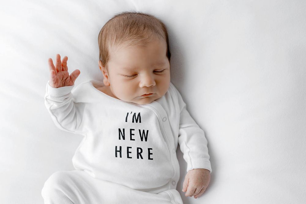 Adorable newborn baby sleeping peacefully in a white onesie that reads I'm New Here.