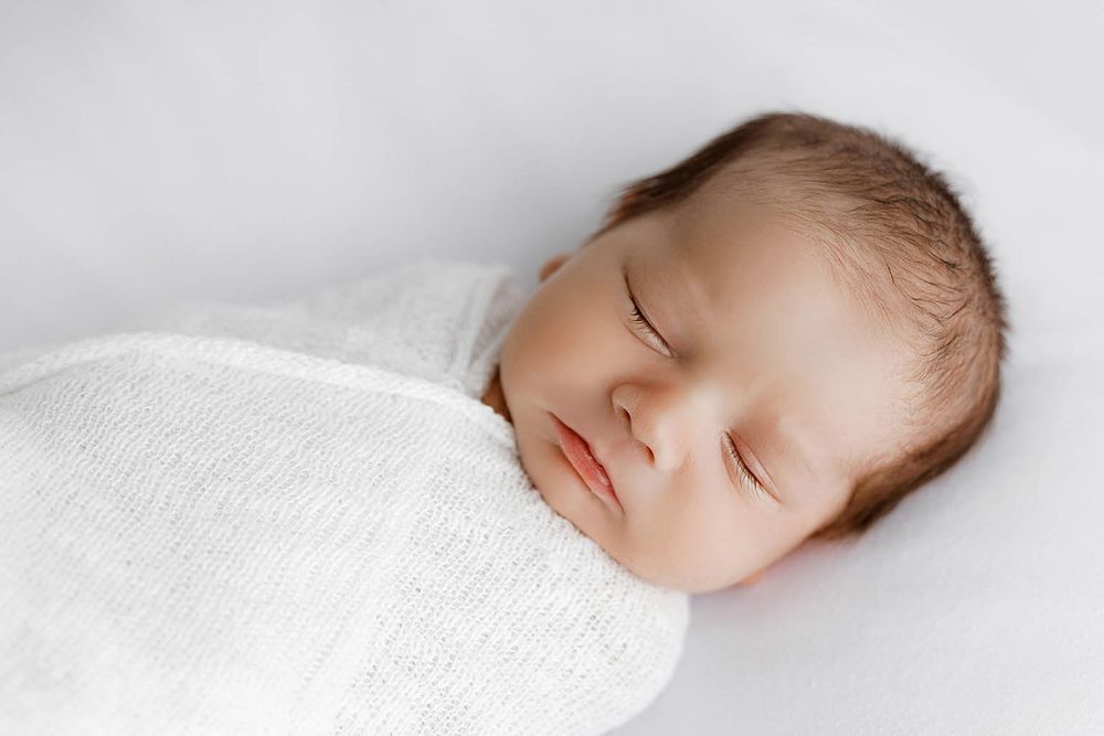 Peaceful newborn baby sleeping soundly swaddled in a soft white wrap blanket.