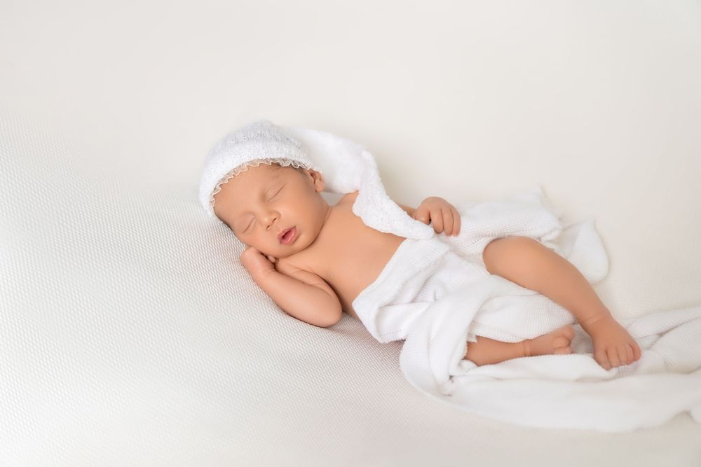 Peaceful newborn baby sleeping in white knit hat and wrap on soft white background.