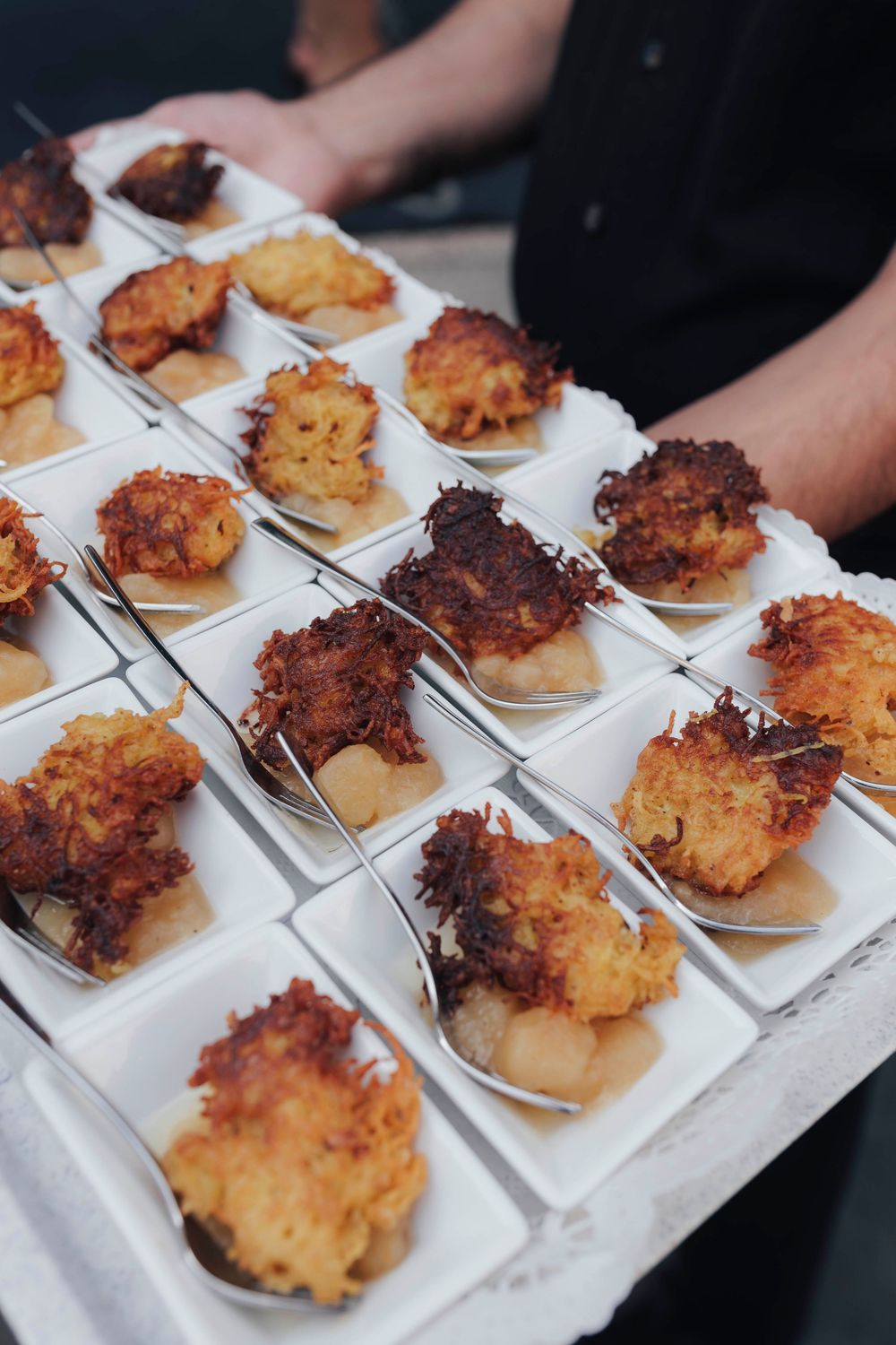 Tray of golden fried coconut shrimp appetizers served on white spoons at a catered event.