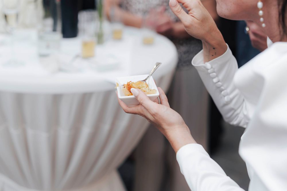 Person in white shirt holding a small dessert cup with a spoon at an elegant catered event.