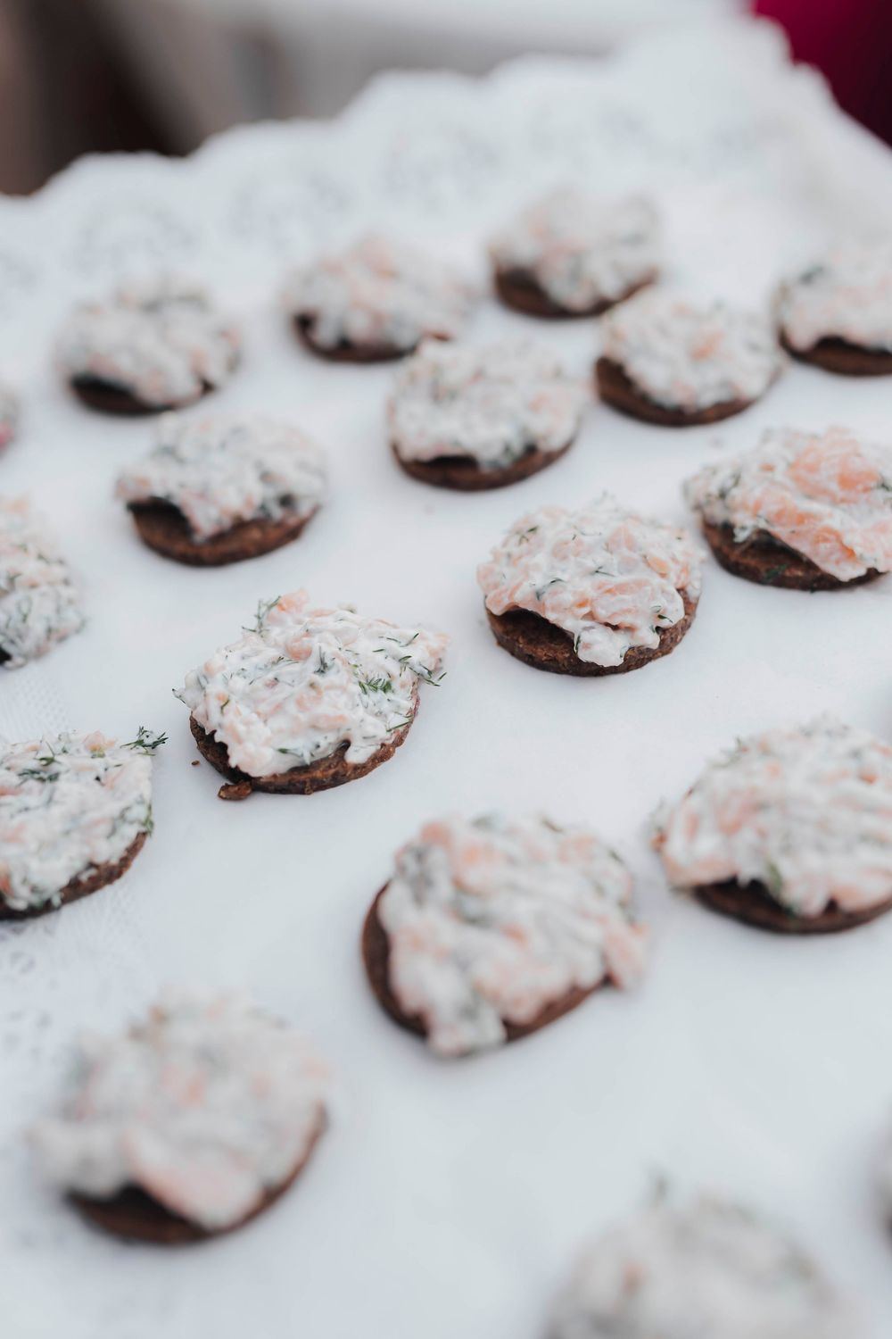 Round dark crackers topped with creamy salmon and dill spread arranged in rows on a white surface.