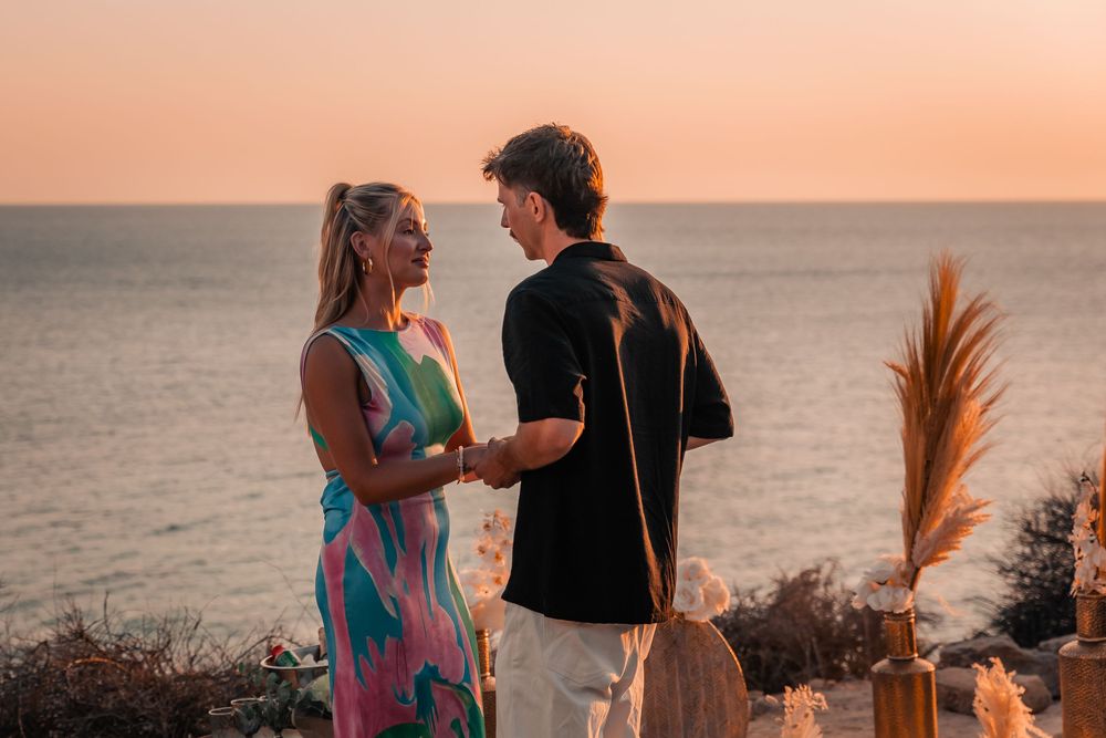 A happy couple holding hands and looking at each other by a boho beach setup after a surprise Mallorca proposal session.