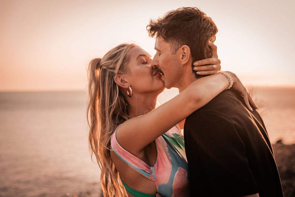 A newly engaged couple sharing a romantic kiss by the sea during a golden hour surprise proposal in Mallorca.