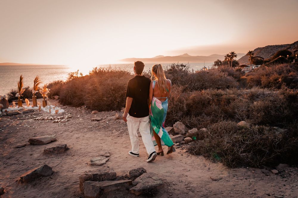 A couple walking together hand-in-hand along a scenic coastal path during a golden hour surprise proposal session in Mallorca.