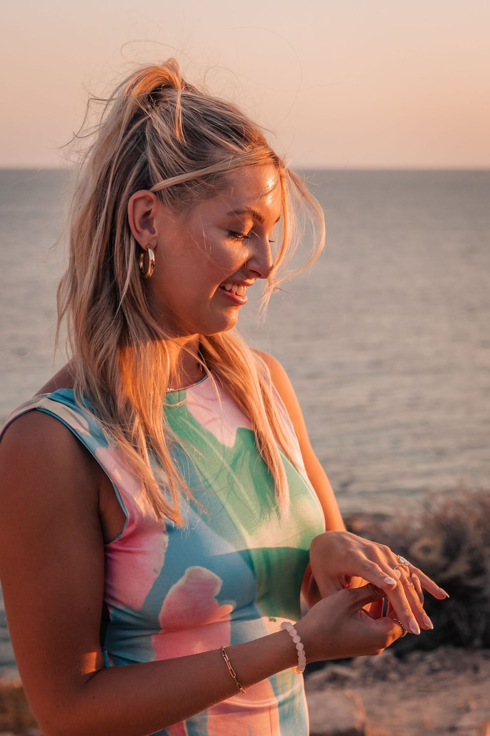 A happy woman smiling down at her engagement ring during a sunset beach surprise proposal session in Mallorca.