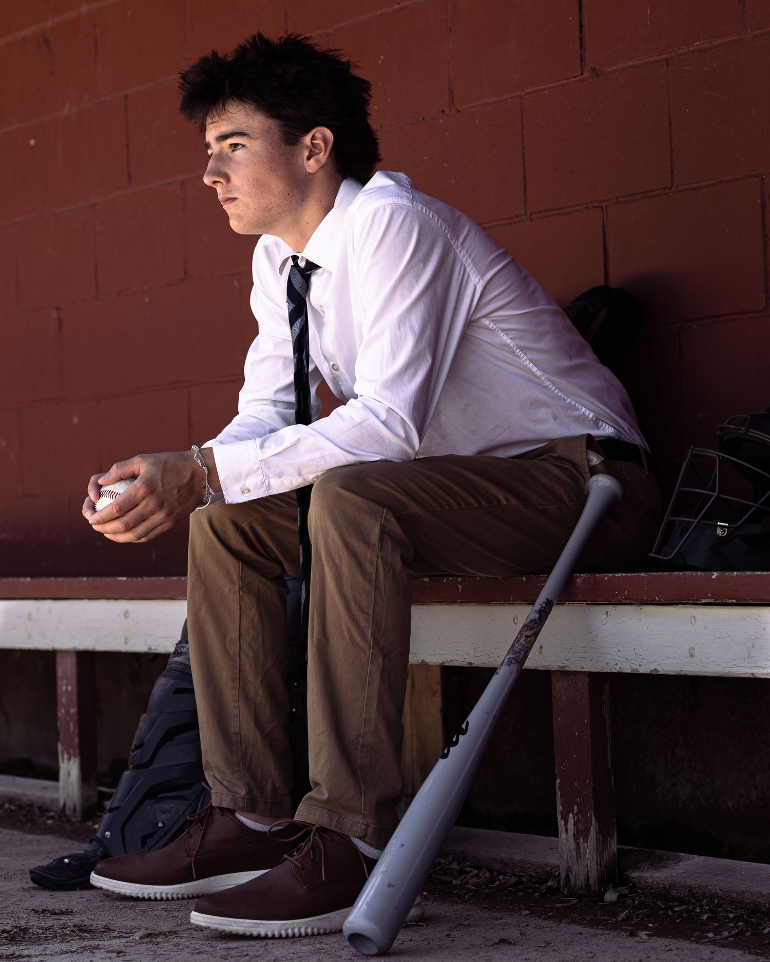 Senior portrait of young man seated in baseball dugout.