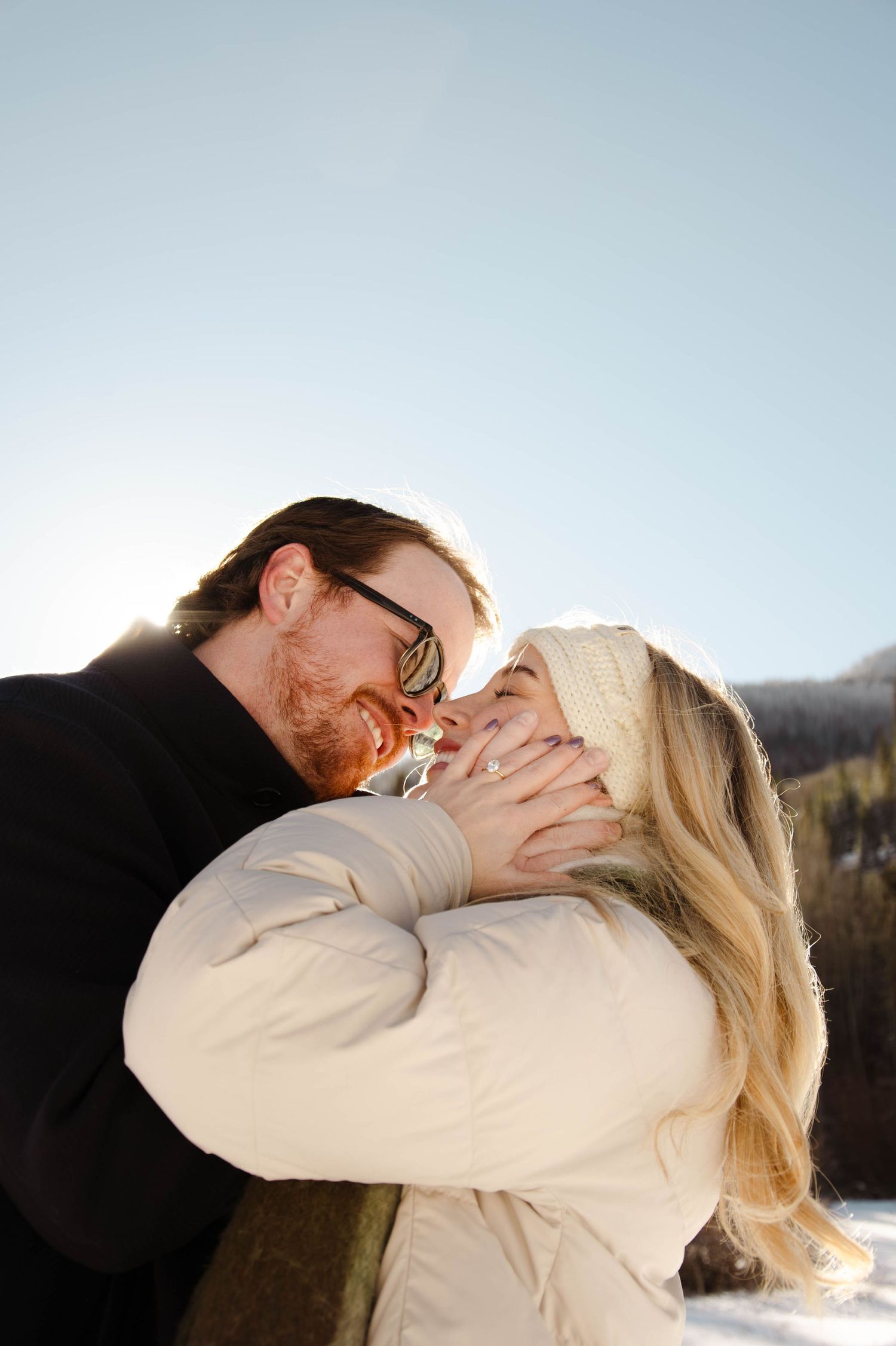Happy couple embracing outdoors in snowy winter landscape on a sunny day.