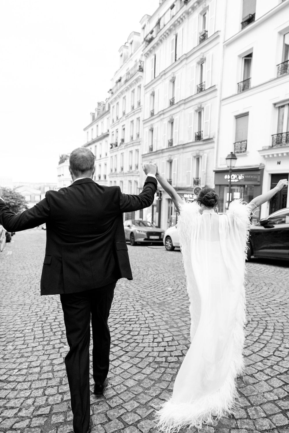 Black and white photo of a bride and groom walking hand in hand on cobblestone streets in Paris.