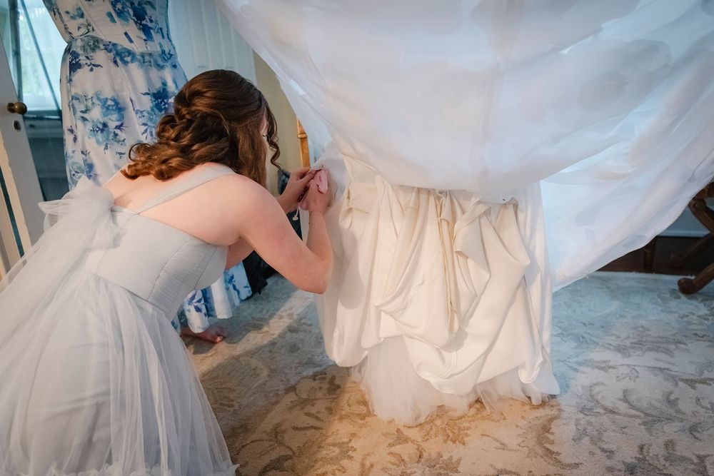 Bridesmaid adjusting the hem of a white wedding dress before the ceremony.