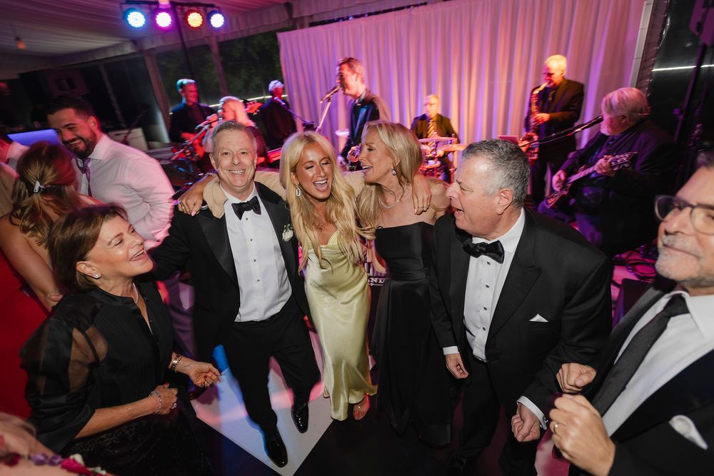 Elegantly dressed guests dancing and socializing at a formal gala event with a live band performing in the background.