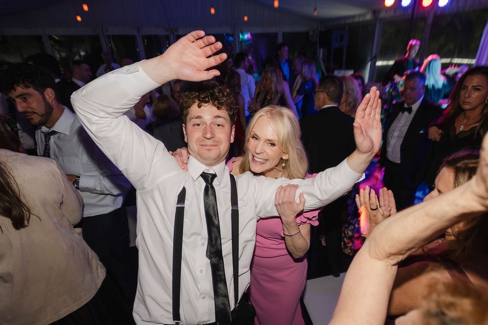 Two guests dancing and smiling at a lively wedding reception party under a white tent.