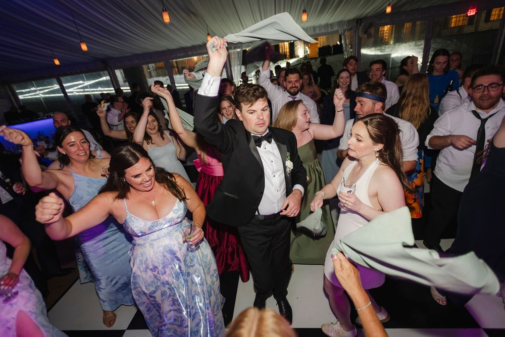 Joyful wedding reception guests dancing energetically in formal attire at an elegant indoor venue.