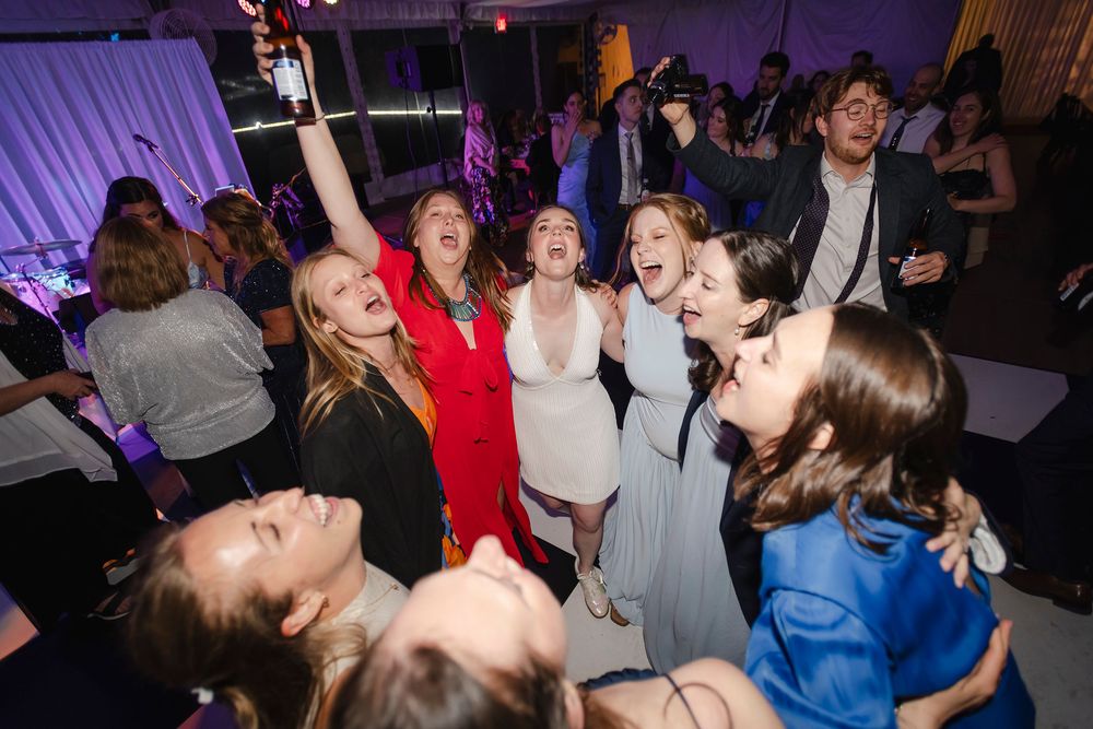 Group of young women dancing and celebrating joyfully at a formal party or wedding reception.