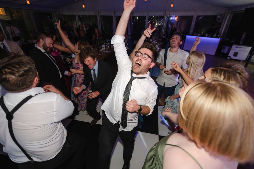 Energetic wedding guest dancing with arms raised on a black and white dance floor at a reception.