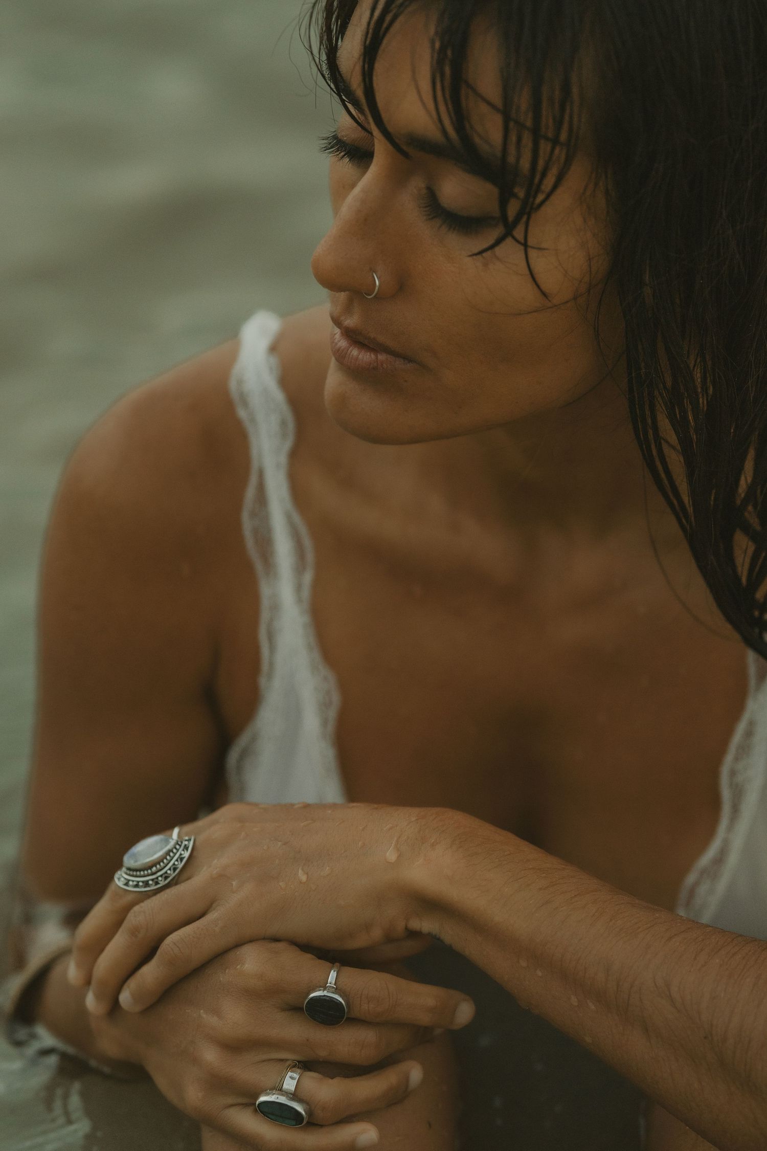 Close-up of a wet-haired woman wearing silver rings with eyes closed near water.